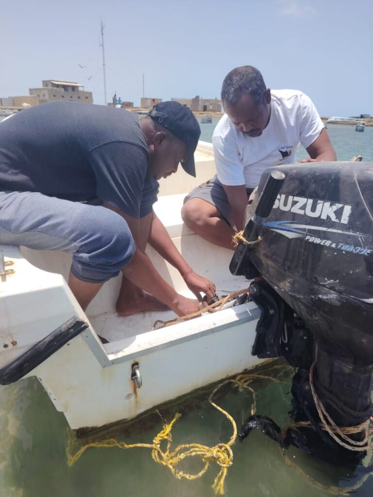 Two WCF officers from the Marine Parks team carry out maintenance work on an outboard boat engine while the vessel is moored in a coastal harbor.