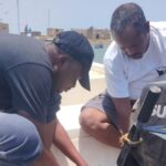 Two WCF officers from the Marine Parks team carry out maintenance work on an outboard boat engine while the vessel is moored in a coastal harbor.