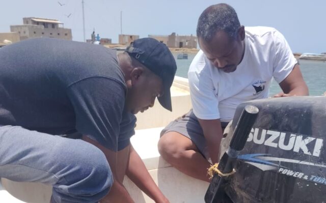 Two WCF officers from the Marine Parks team carry out maintenance work on an outboard boat engine while the vessel is moored in a coastal harbor.